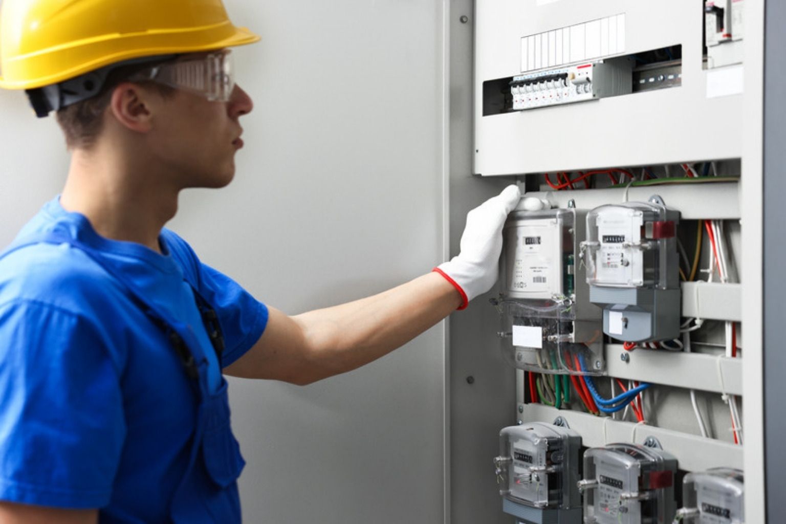 Elektriker med hjelm og handsker tjekker en åben eltavle med målere